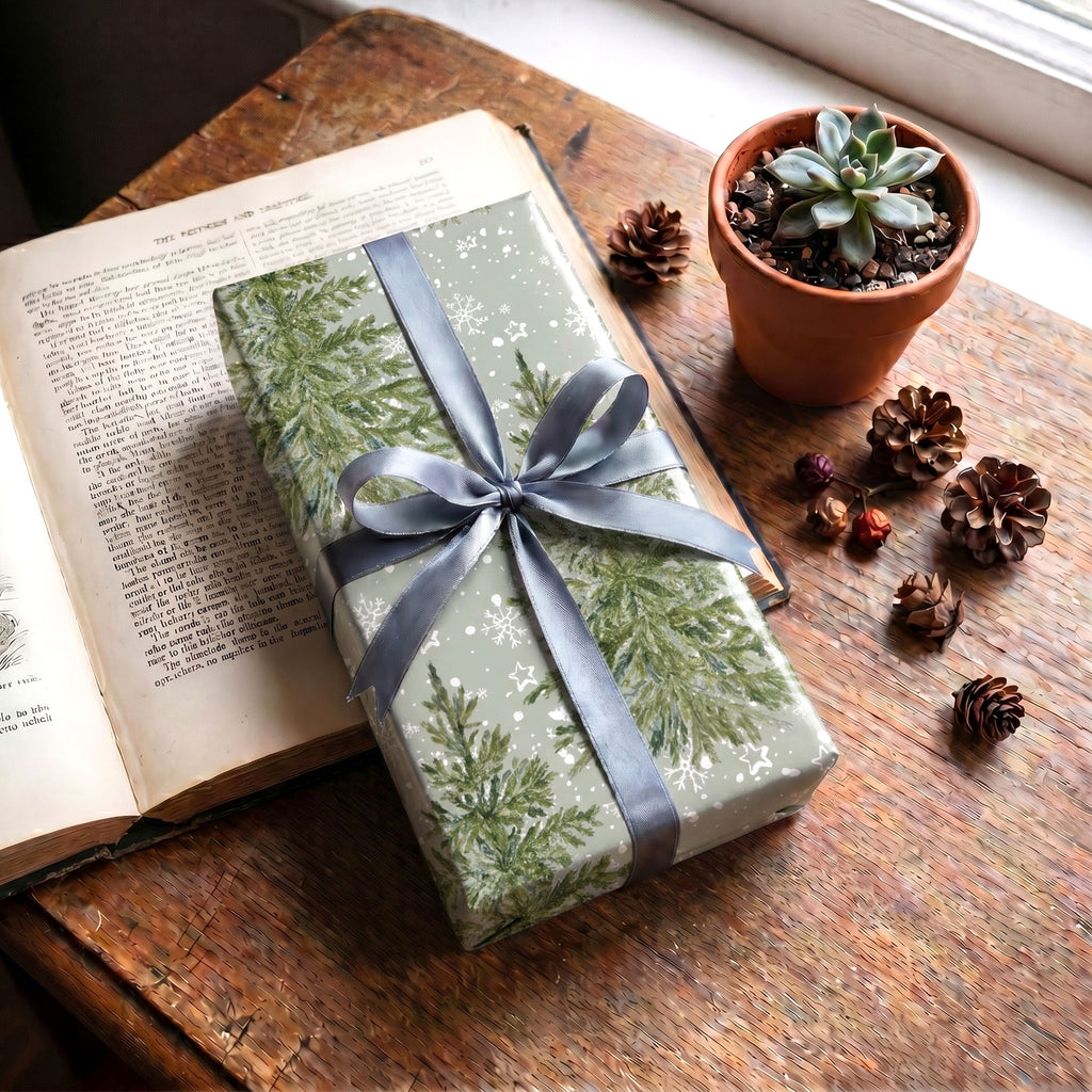 Gift wrapped in Sage Pine Trees paper with a blue-grey ribbon, on an open book