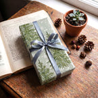 Gift wrapped in Sage Pine Trees paper with a blue-grey ribbon, on an open book